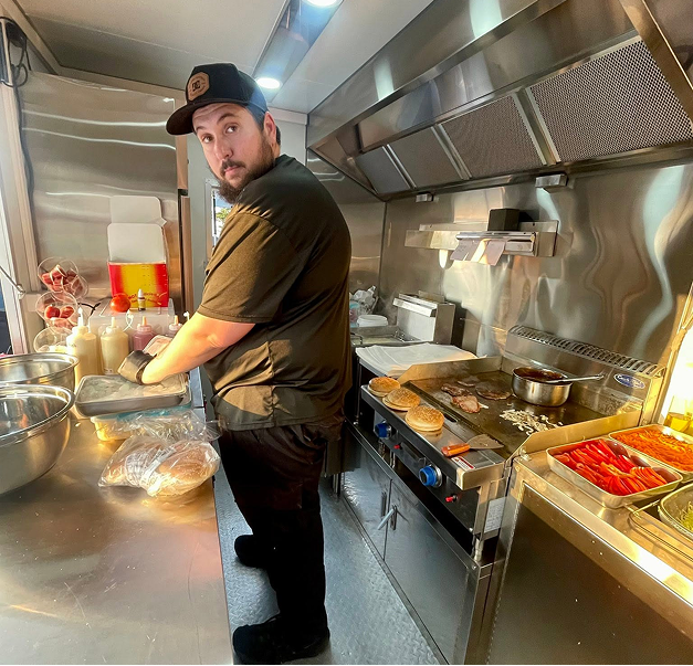 Mully & Lou's chef working the grill — patties, bacon and eggs cooking